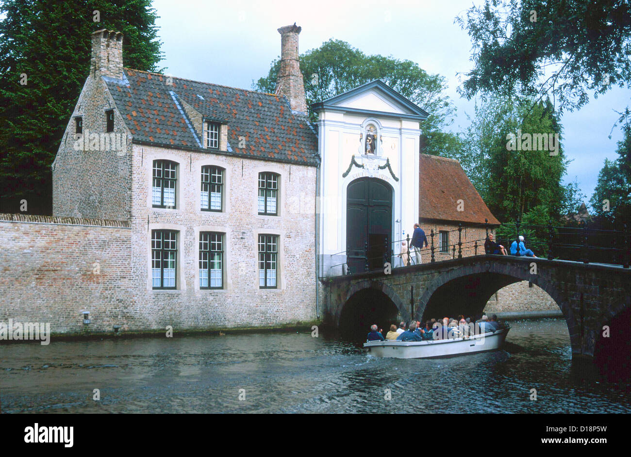 Bruges Belgium+ A boat load of tourists travel under a bridge by th entrance to the Beguinage Convent Stock Photo