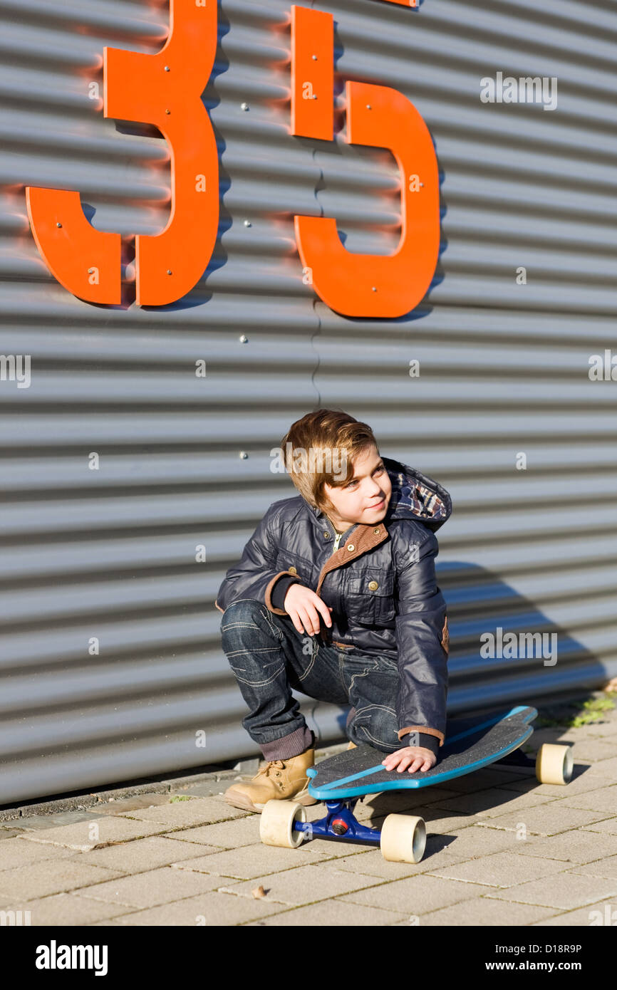 Portrait of boy crouching on a skateboard in front of metal fence Stock Photo