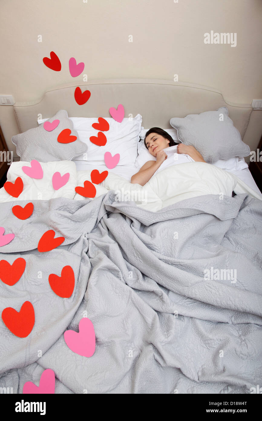 Woman asleep in bed with heart shapes on bedclothes Stock Photo