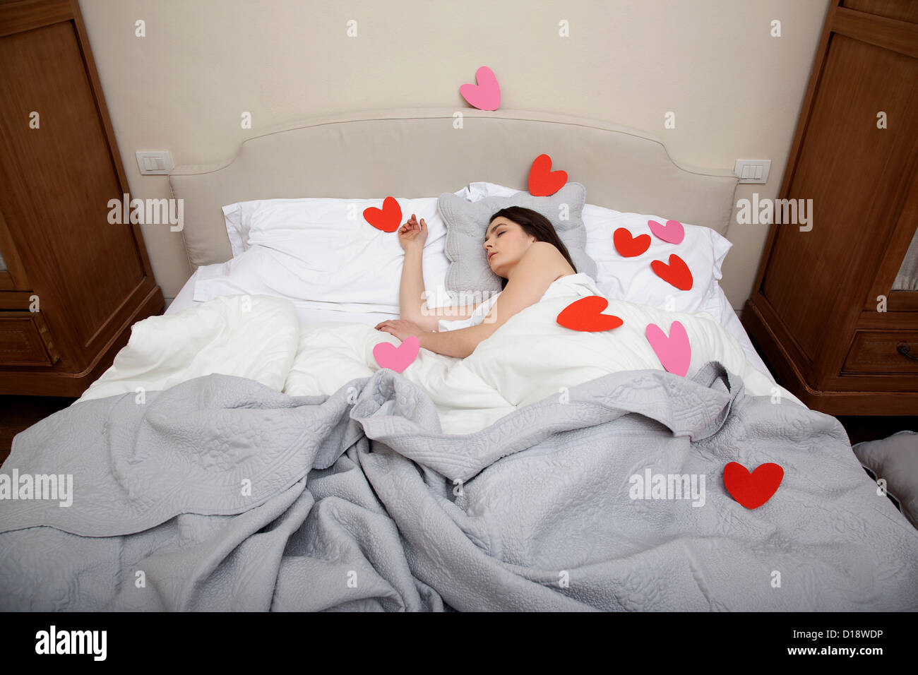 Woman asleep in bed with heart shapes on bedclothes Stock Photo