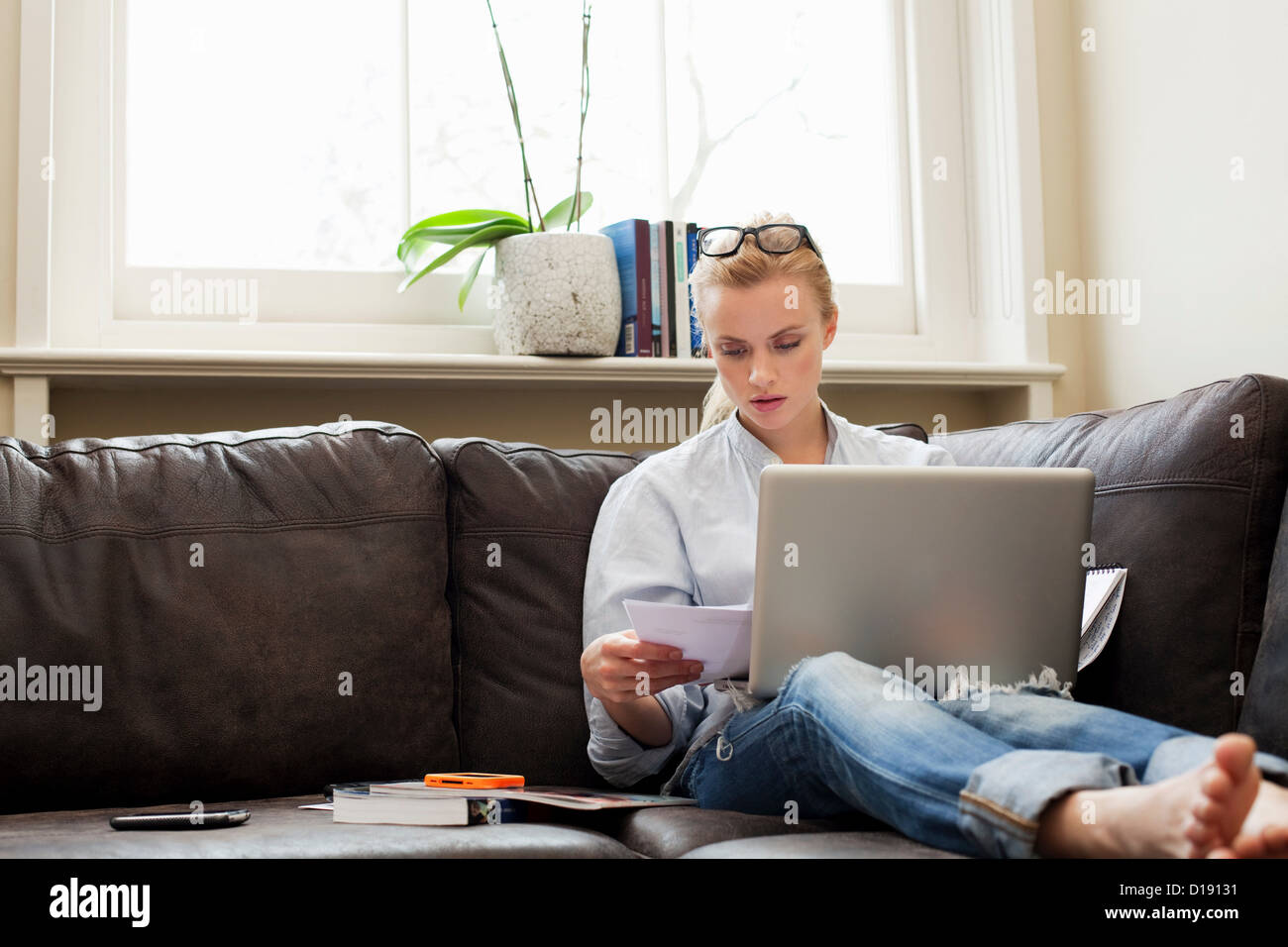 Young woman sitting on sofa with laptop and papers Stock Photo