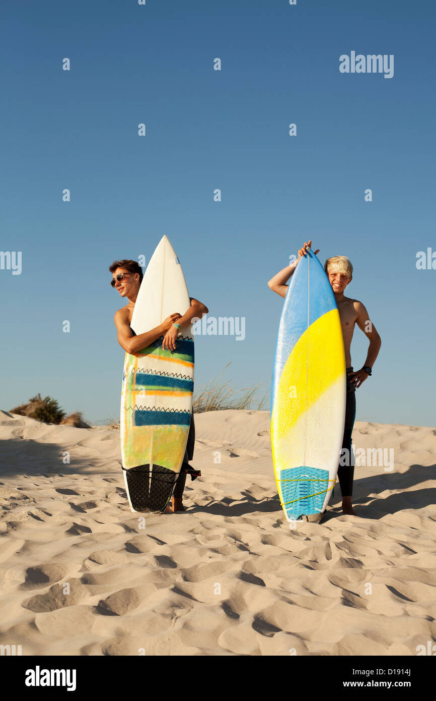 Two young men standing behind surfboards on beach Stock Photo
