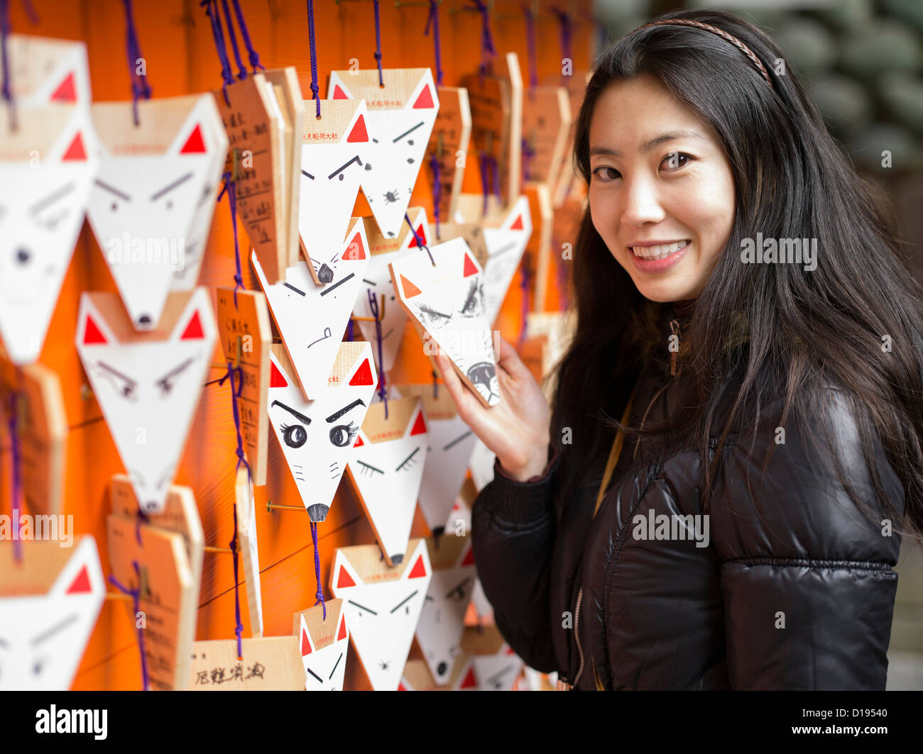 Japanese woman visiting Fushimi Inari Taisha a shinto shrine with orange torii gates in Kyoto, Japan. Fox shaped prayer ema Stock Photo