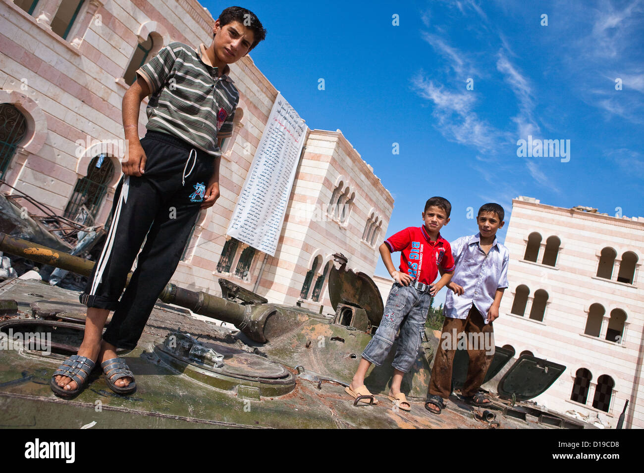 Azaz, Syria, 5/10/12. Kids on top of a disabled tank outside the damaged mosque in Azaz. Banner in background names martyrs. Stock Photo