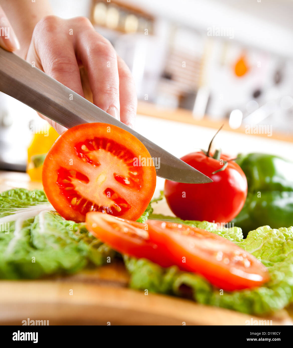 Woman's hands cutting tomato, behind fresh vegetables. Stock Photo