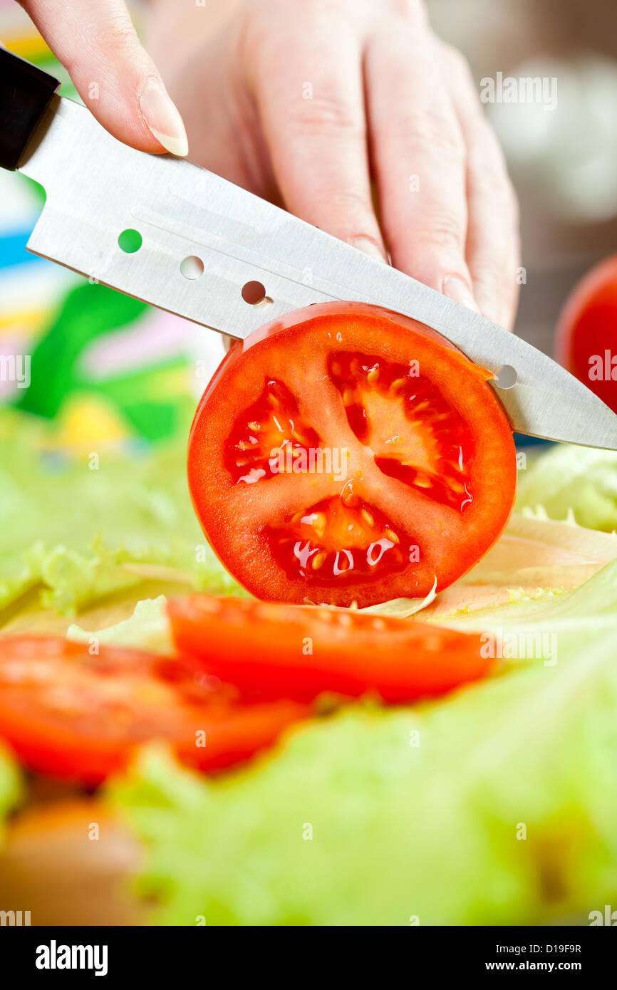 Woman's hands cutting tomato, behind fresh vegetables. Stock Photo