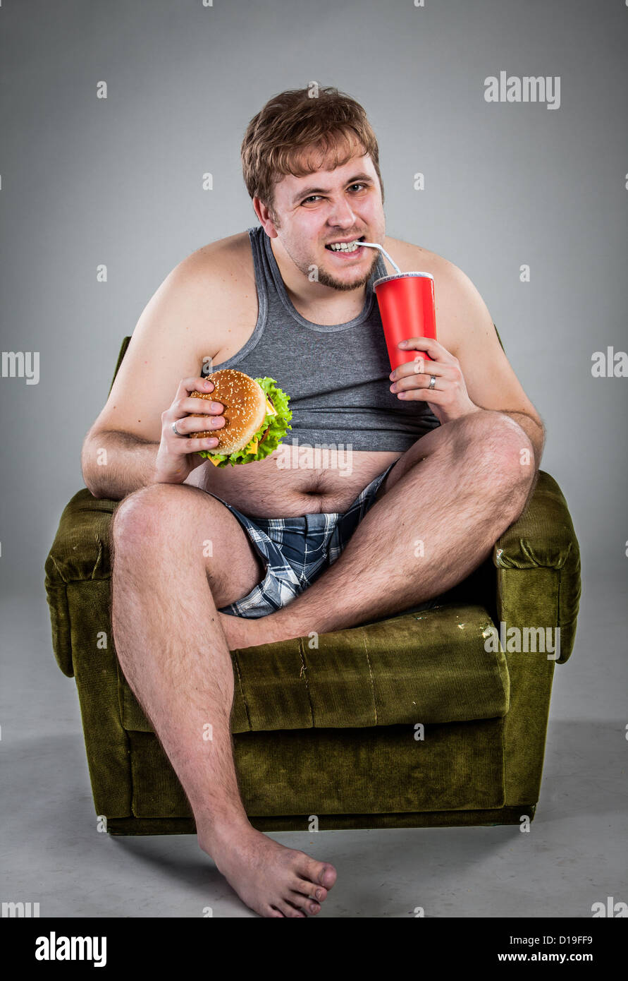 fat man eating hamburger seated on armchair Stock Photo