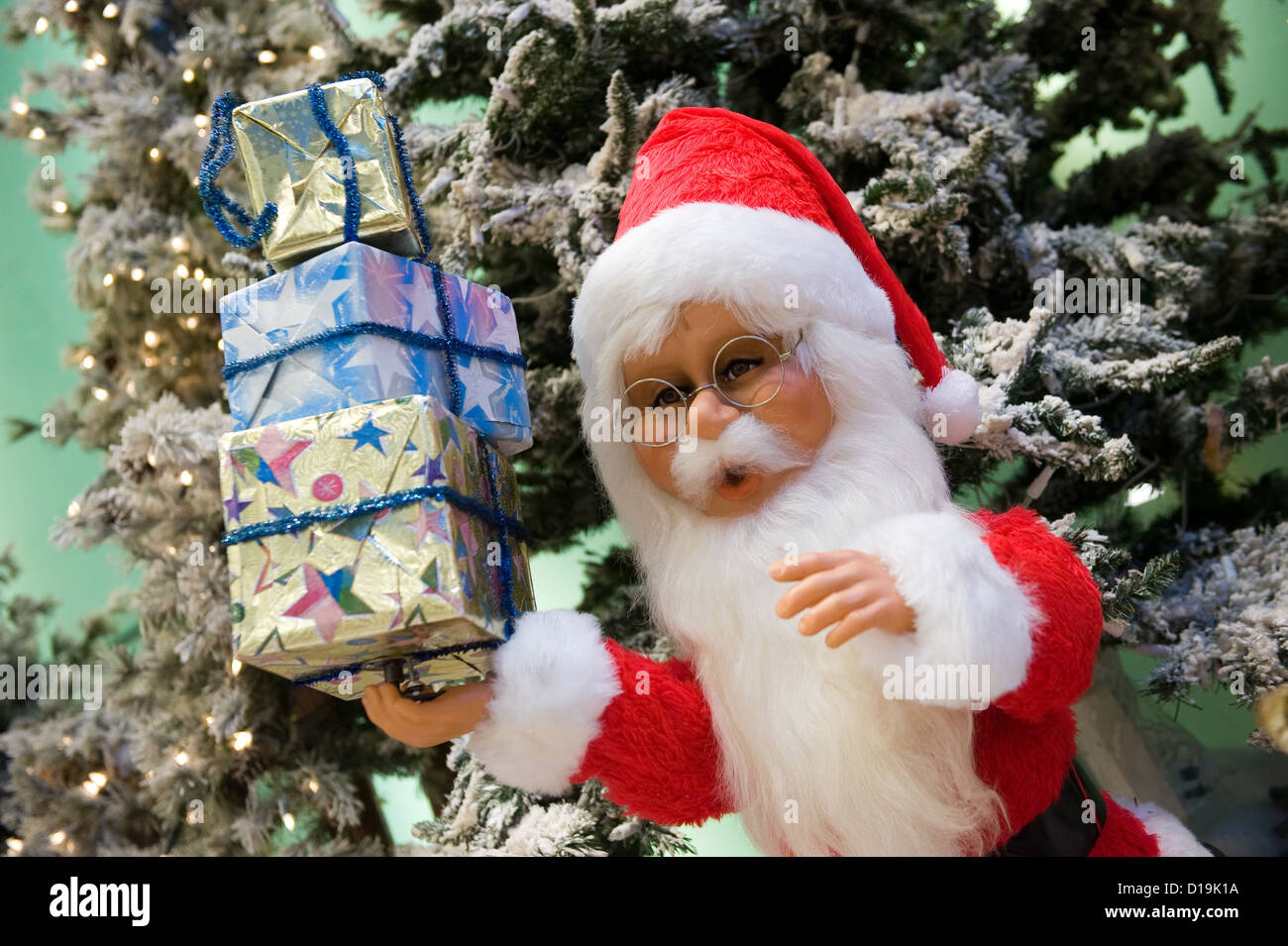 Santa Claus doll carrying 3 presents before a christmas tree Stock Photo