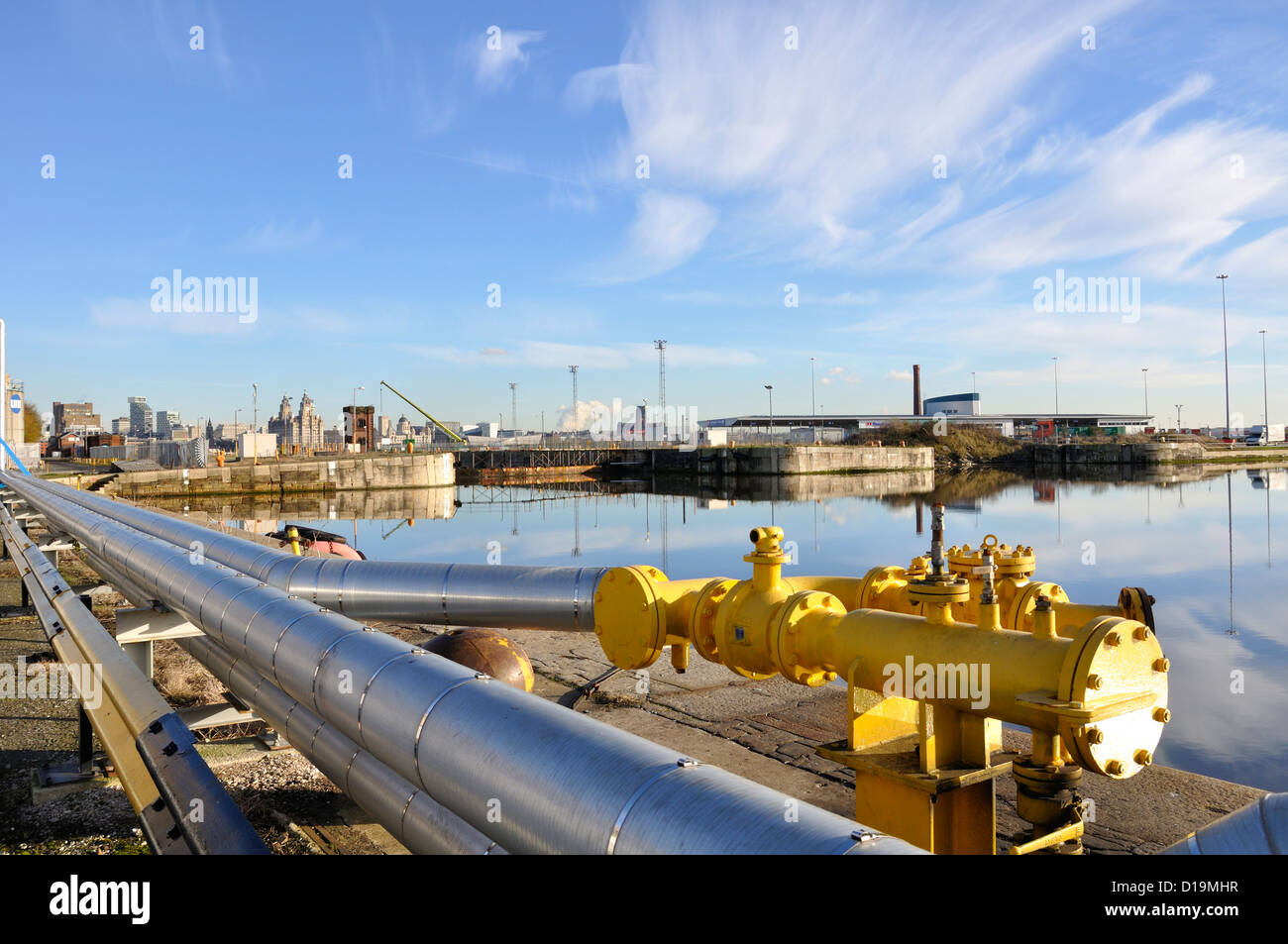 A silver pipeline runs alongside the quay at Wallasey. The Liverpool skyline is in the distance and the Liver Birds building Stock Photo