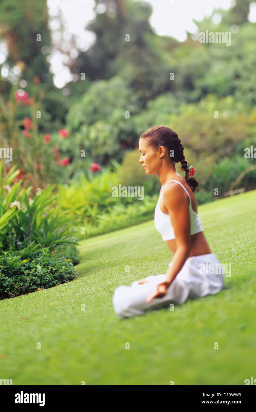 Woman Sitting On Grass Doing Yoga In A Tropical Garden Stock Photo - Alamy