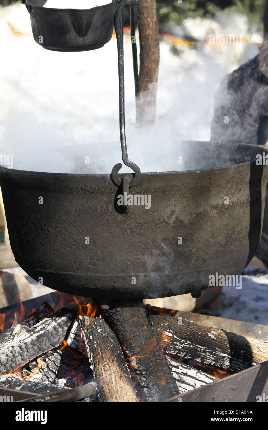 Big kettles over an open wood fire, boiling maple sap outdoors to