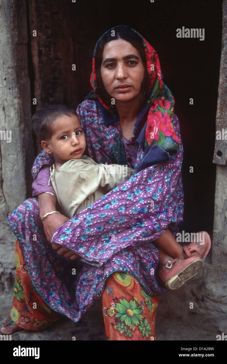 Kashmir - a mother holds her small boy child on her knee, she is dressed in traditional, brightly-coloured clothes. Both look directly at the camera Stock Photo