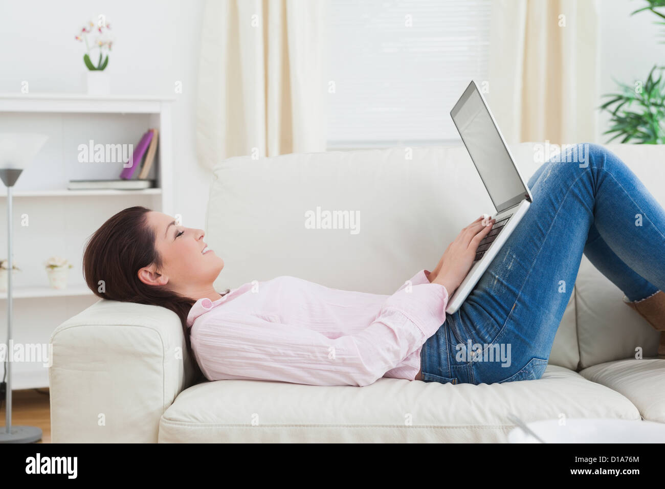 Happy woman lying on sofa and using laptop Stock Photo - Alamy