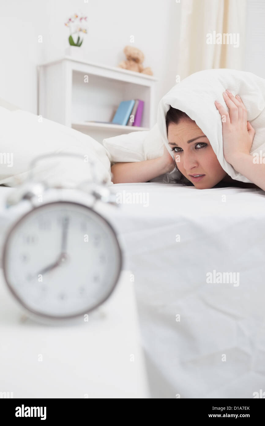 Woman covers ears with sheet as alarm clock rings Stock Photo Alamy