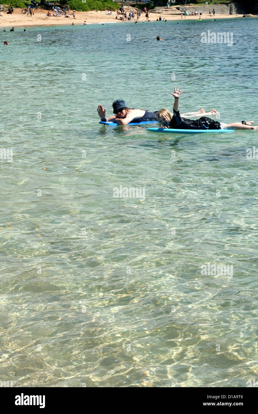 Woman and girl paddling on boogie boards in clear blue water of Kapalua