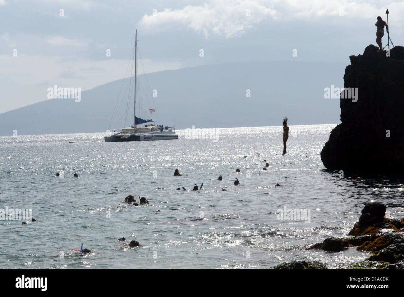 Seascape of silhouettes of snorkelers, cliff jumpers and catamaran tourists at Black Rock Beach, Maui Island, Hawaii, USA Stock Photo