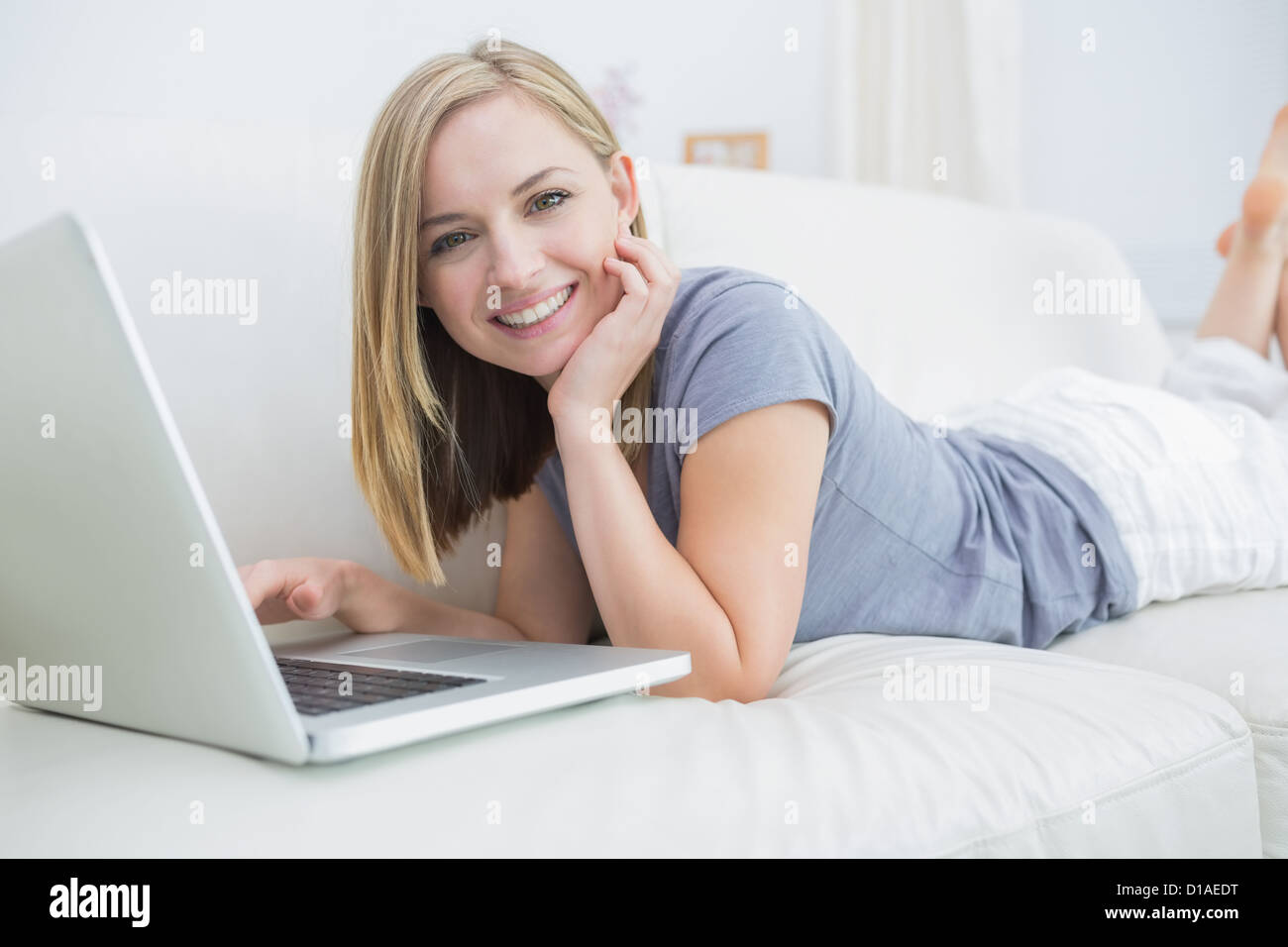 Young woman lying on couch and using laptop Stock Photo - Alamy