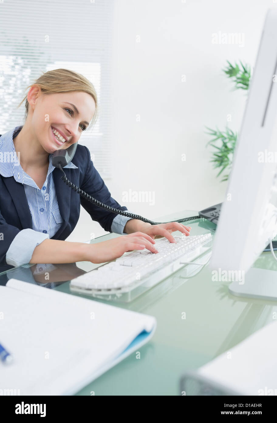 Female executive using landline phone and computer at desk Stock Photo