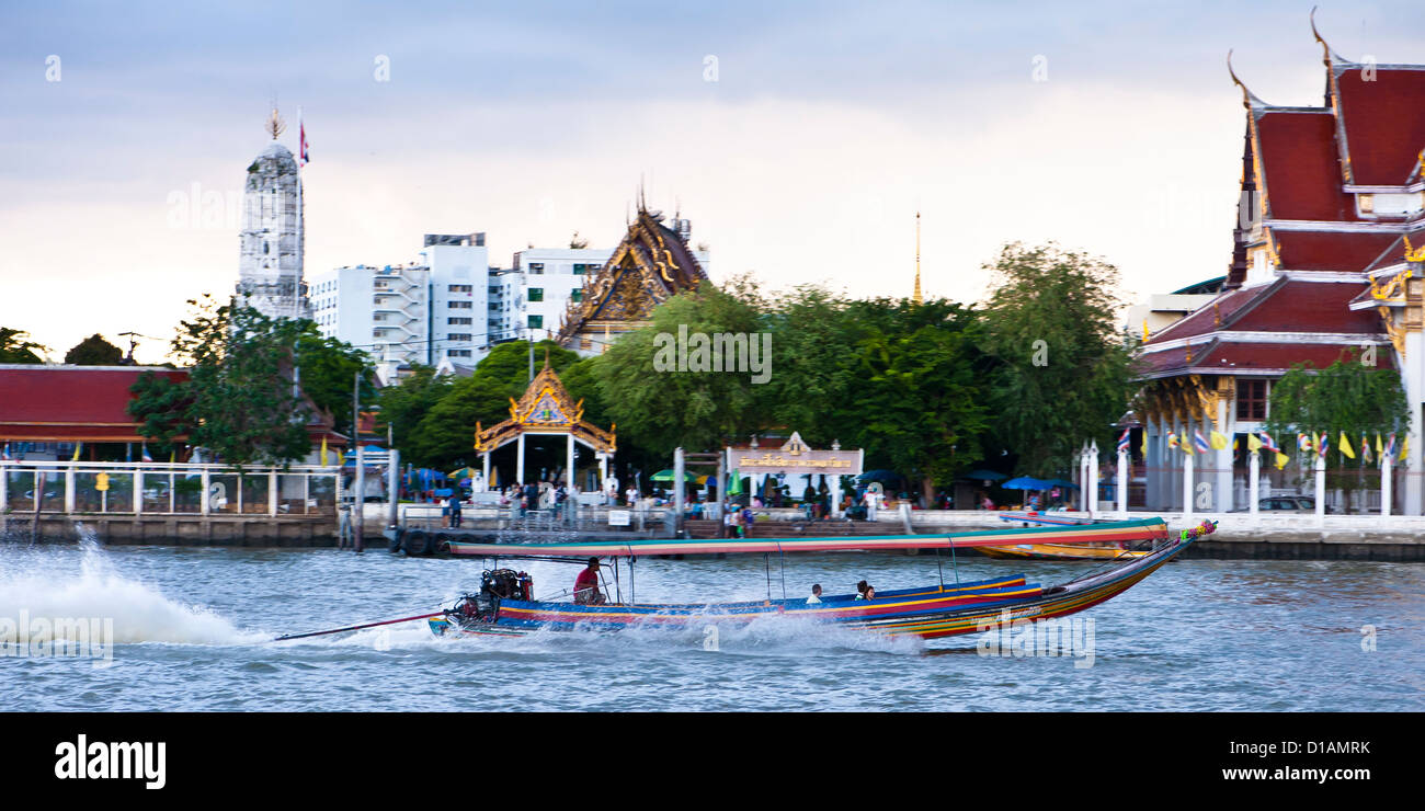A long tail boat speeds past the  temple of Bells on the Chao Phraya, Bangkok Stock Photo