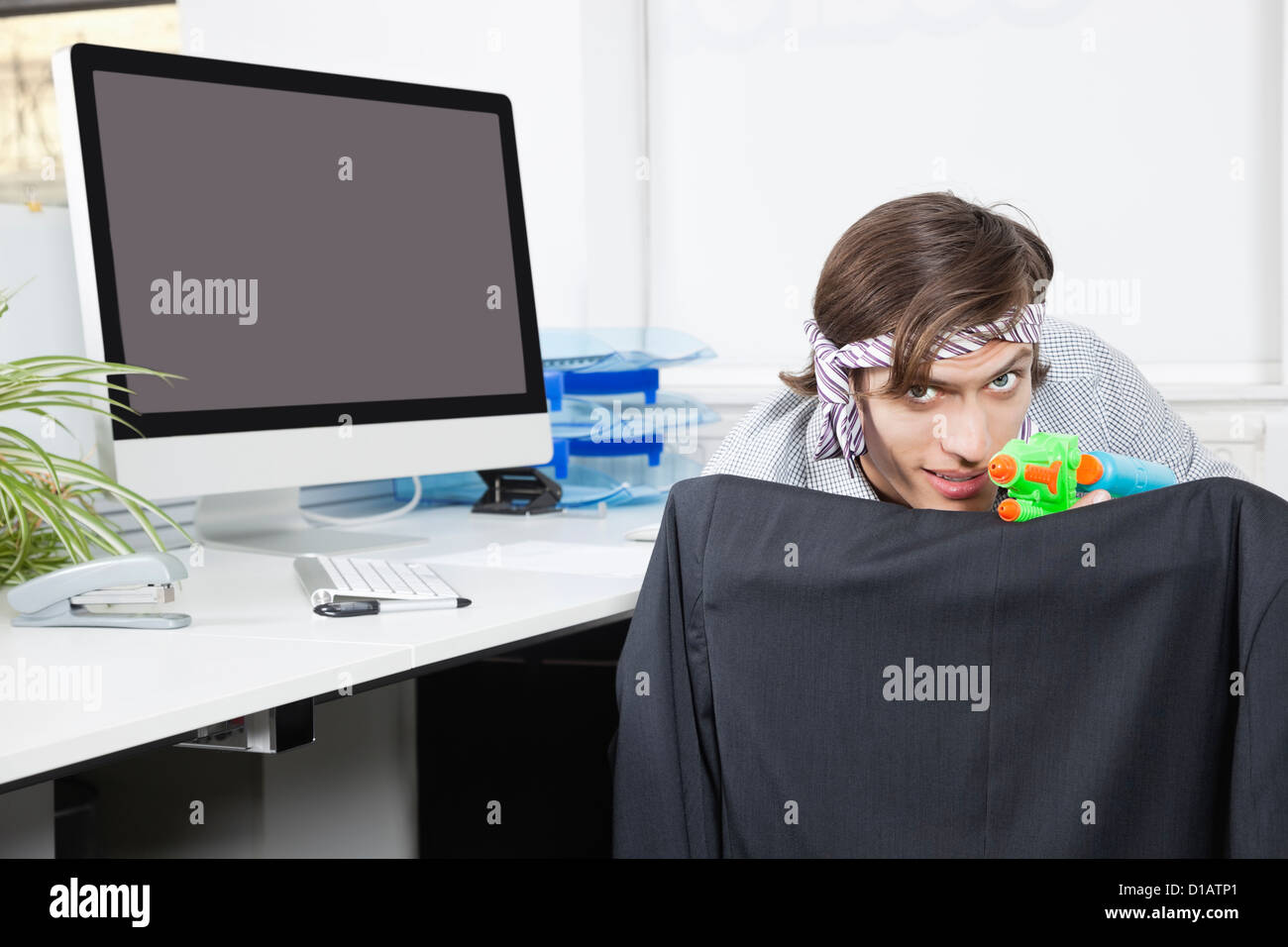Portrait young businessman aiming toy gun at desk Stock Photo