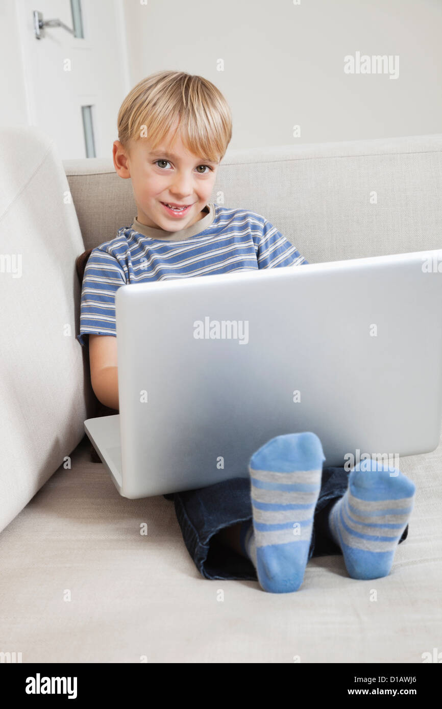 Portrait happy young boy using laptop on sofa Stock Photo - Alamy