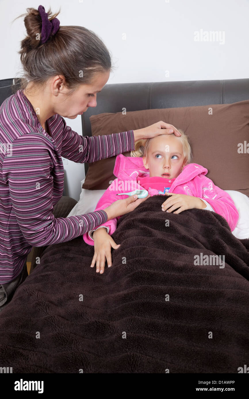 mother checking unwell girl's temperature at home Stock Photo