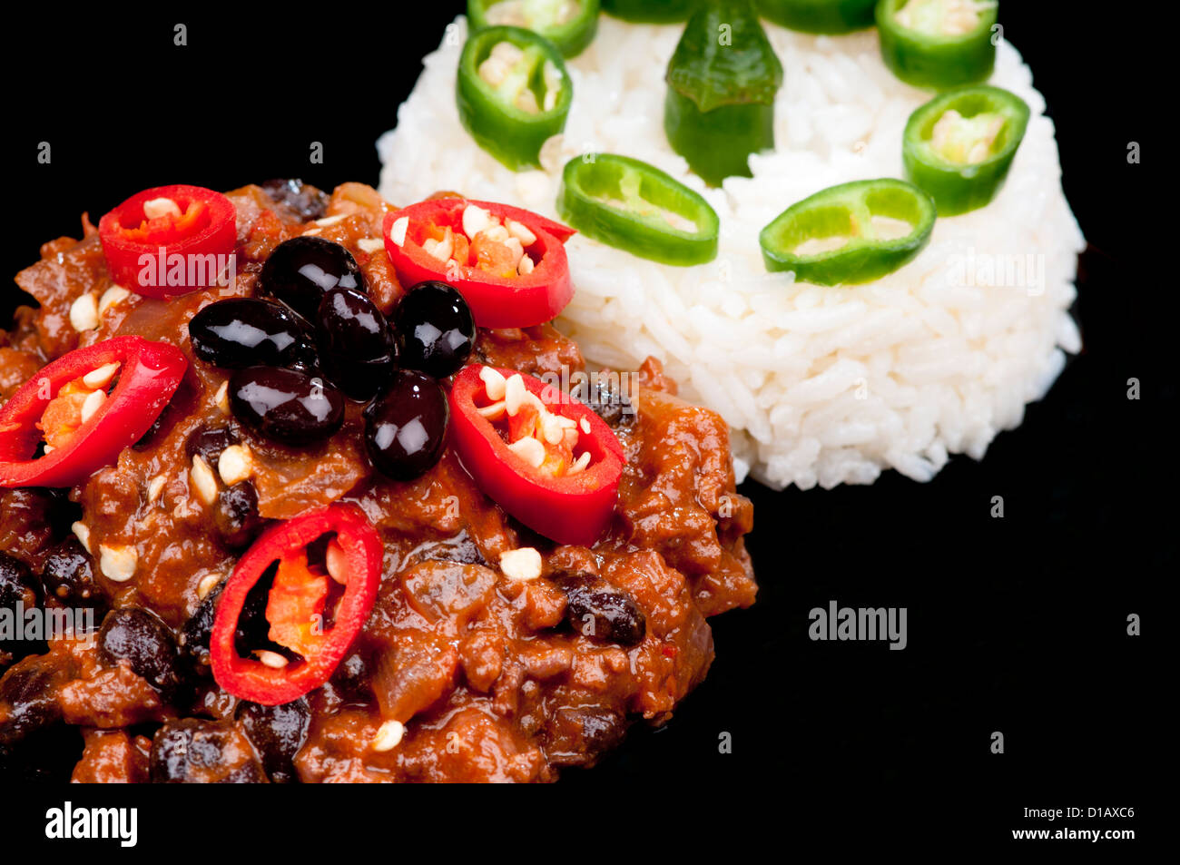 Hot and spicy Chili con Carne garnished with red peppers and rice with green pepper. On black Stock Photo