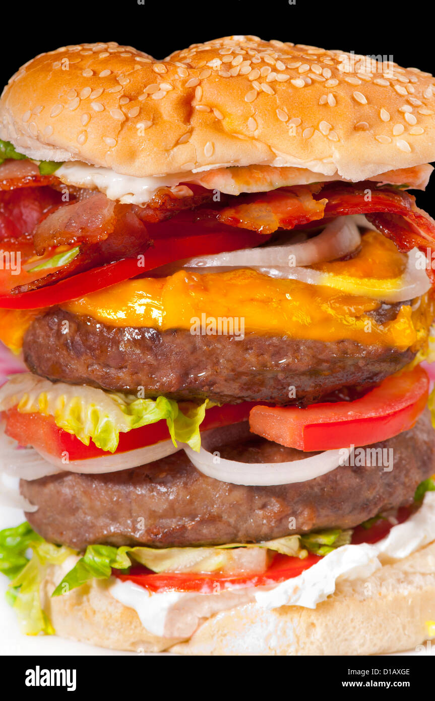 Giant double hamburger with tomato slices, cheese, cream cheese, bacon, egg, lettuce and onion in a white bread bun Stock Photo