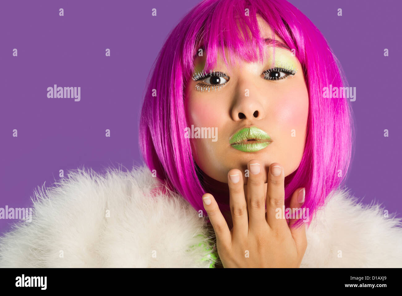 Portrait young funky woman in pink wig blowing kiss over purple background Stock Photo