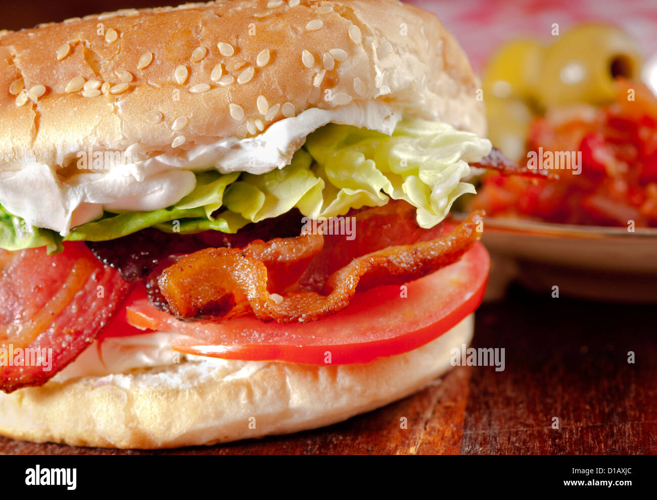 BLT  Bacon, lettuce, tomato and cream cheese sandwich in a bun with olives and pickle in the background Stock Photo