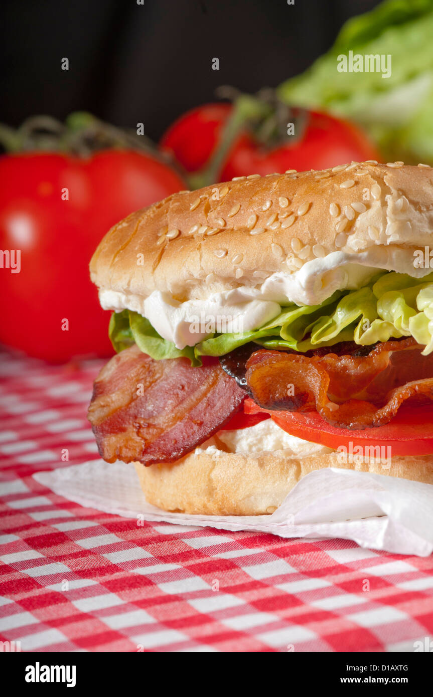 BLT  Bacon, lettuce, tomato and cream cheese sandwich in a bun with tomato and lettuce in the background with  red check cloth Stock Photo
