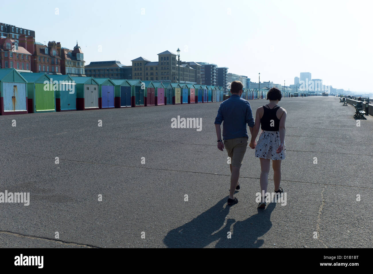 Couple holding hands walking in sunshine,Hove promenade,beach huts Stock Photo