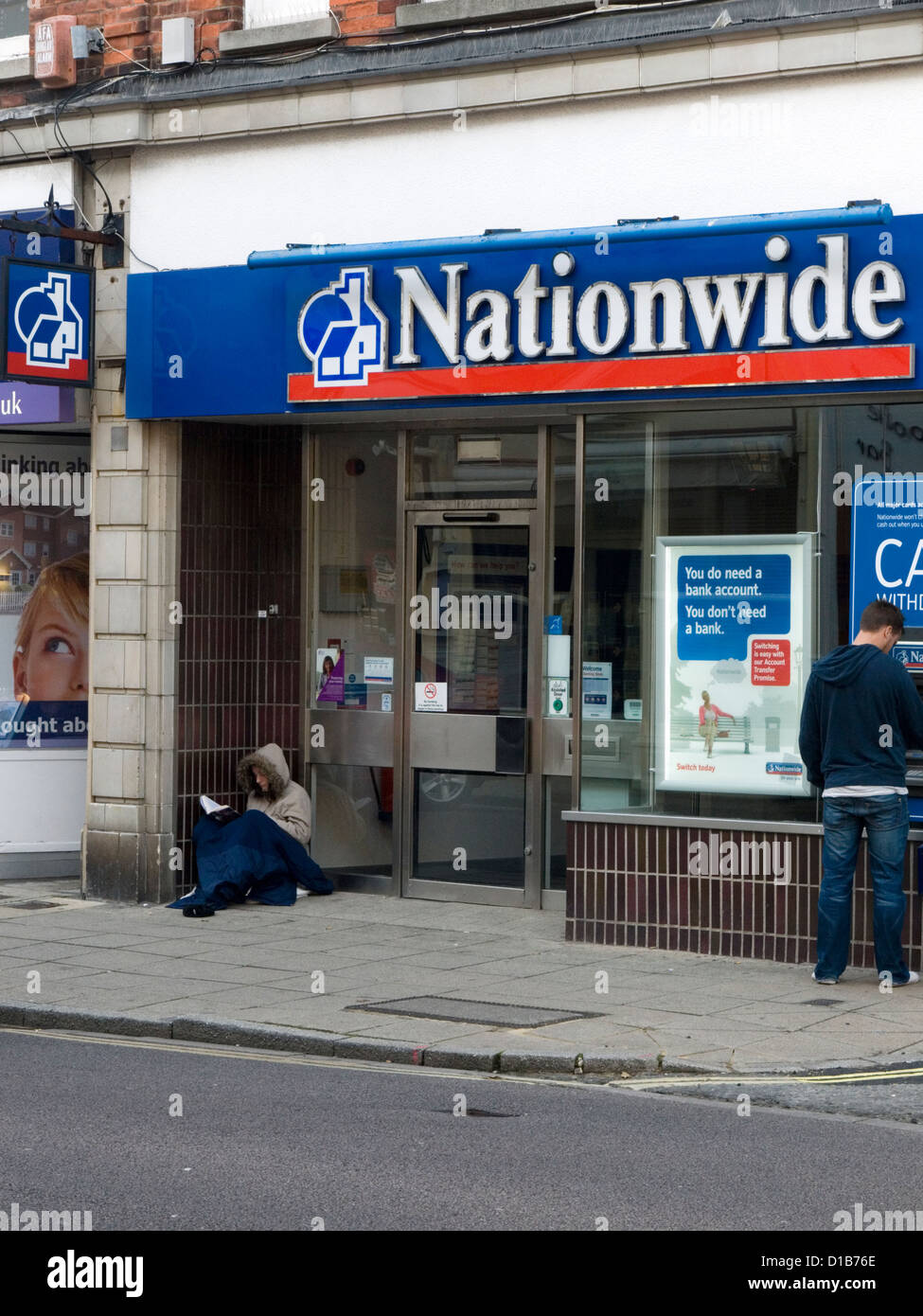 homeless woman begging on the street outside of a bank and letting agency Stock Photo