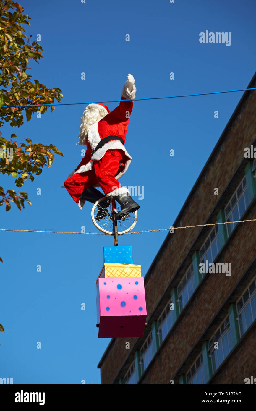 Model of Father Christmas cycling along tight rope wire on monocycle with presents at Bournemouth Town Centre in December Stock Photo