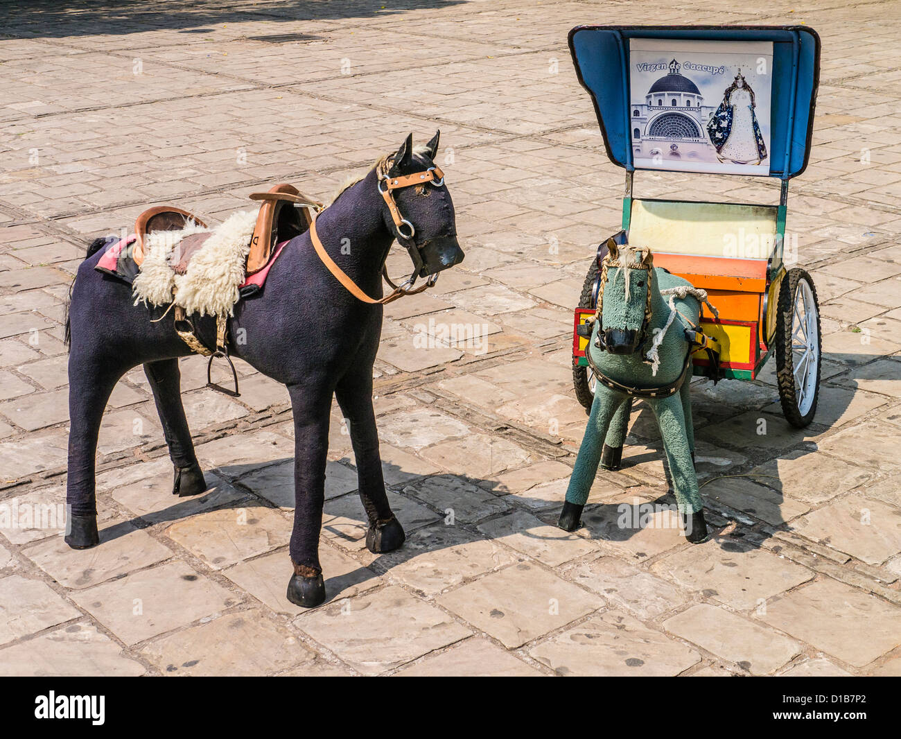 A miniature horse with saddle and a smaller pony pulling a cart, both stuffed animals, on the
