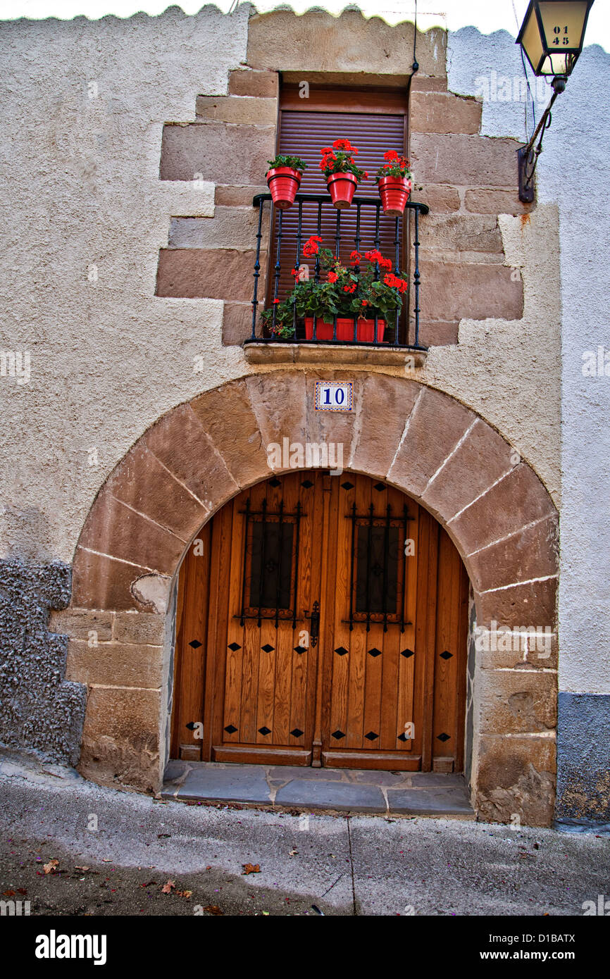 Arched wooden door and doorway, with geranium planters in the window above it, Rural Spain Stock Photo