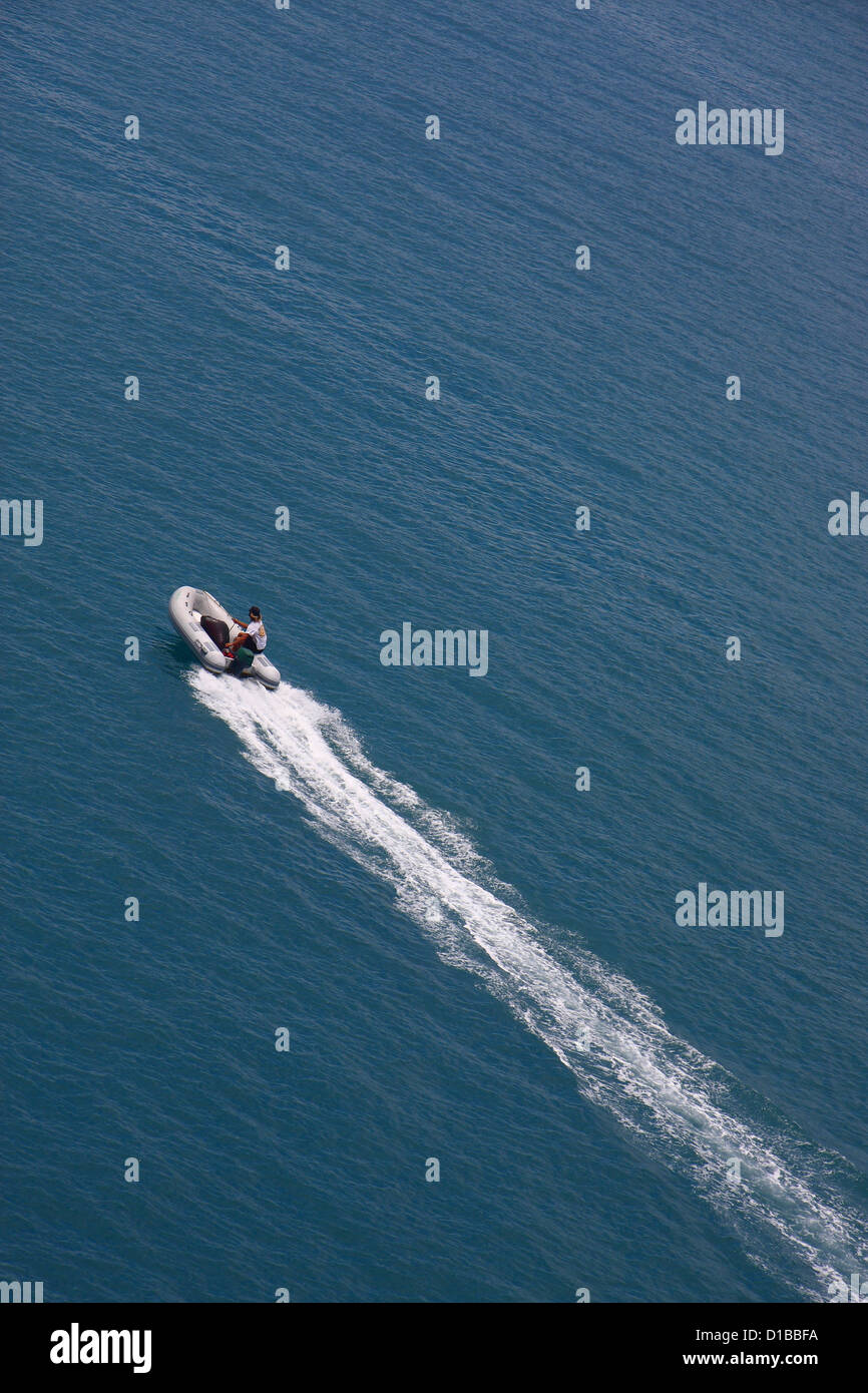 A man speeding across blue water in a gray rubber dinghy Stock Photo ...
