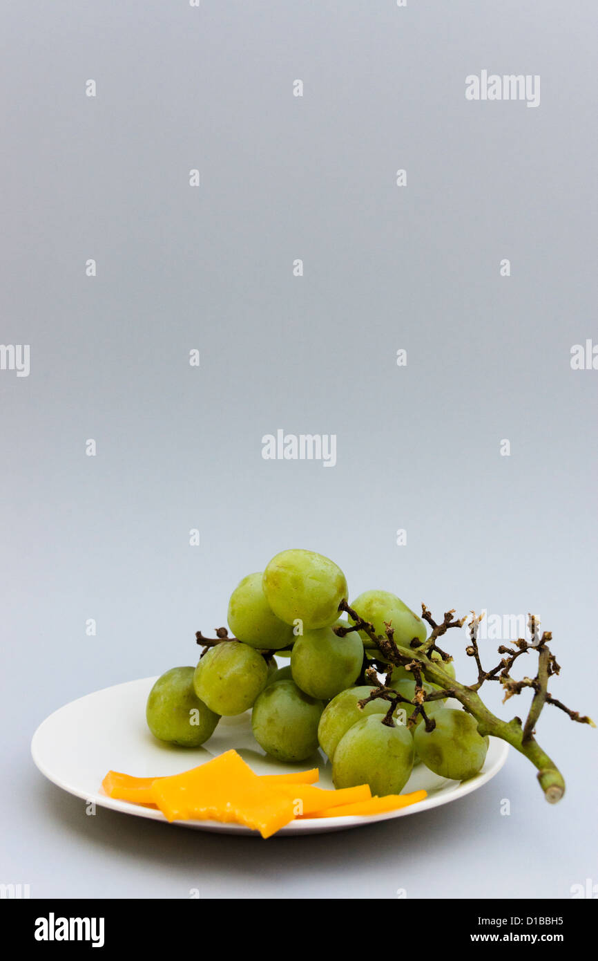 Green seedless grapes and sliced cheddar cheese on a small plate Stock