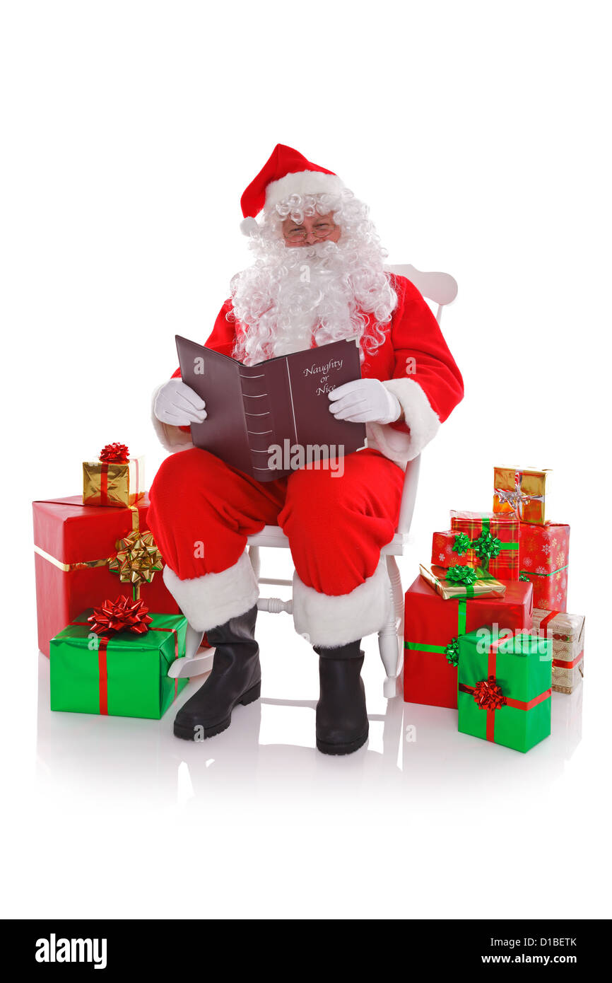 Santa Claus sat in a rocking chair surrounded by gift wrapped presents as he reads the Naught or Nice list Stock Photo