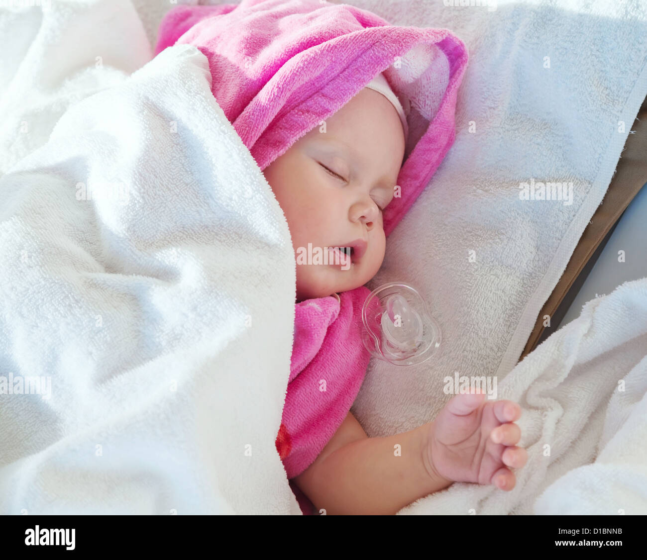 Baby girl sleeps under pink and white cotton towels with a pacifier nearby Stock Photo