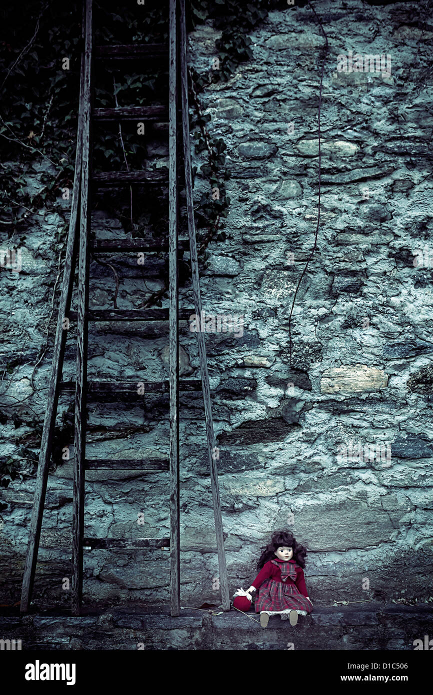 an old doll sitting on a wall next to an old wooden ladder Stock Photo