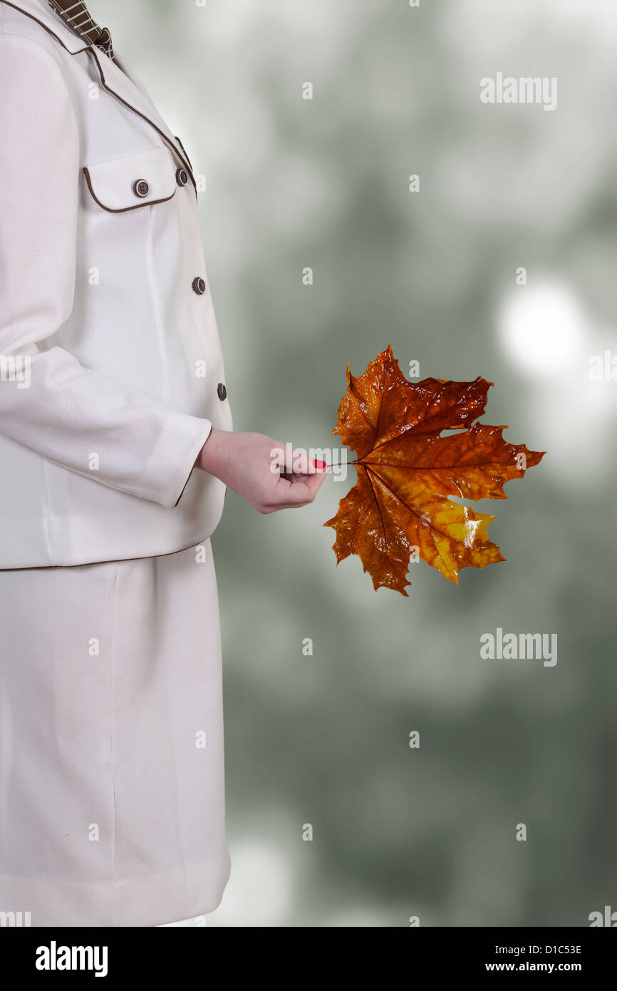 a woman in a white skirt suit is holding an autumnal red leaf from a sycamore tree Stock Photo