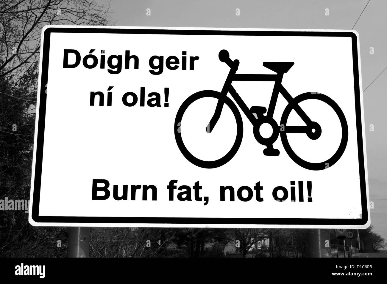 burn fat not oil irish road sign on a quiet road entering a town in ireland in black and white Stock Photo