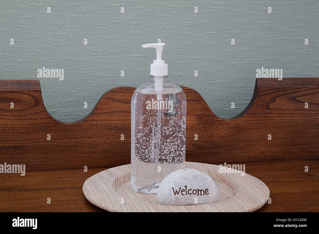 Hand Sanitizer and welcome sign on beige linen plate, antique oak table with green linen background. Help yourself stay healthy. Stock Photo