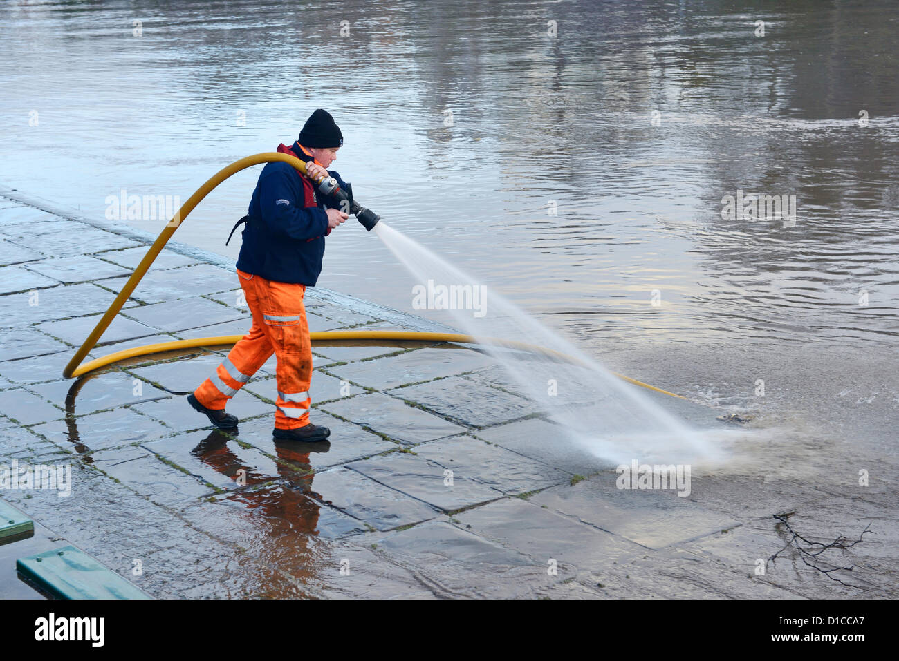 A worker washes mud and silt from the pavement at The Groves in Chester which was caused by the heavy rain the previous day in Wales making the river level through Chester much higher than normal. Stock Photo
