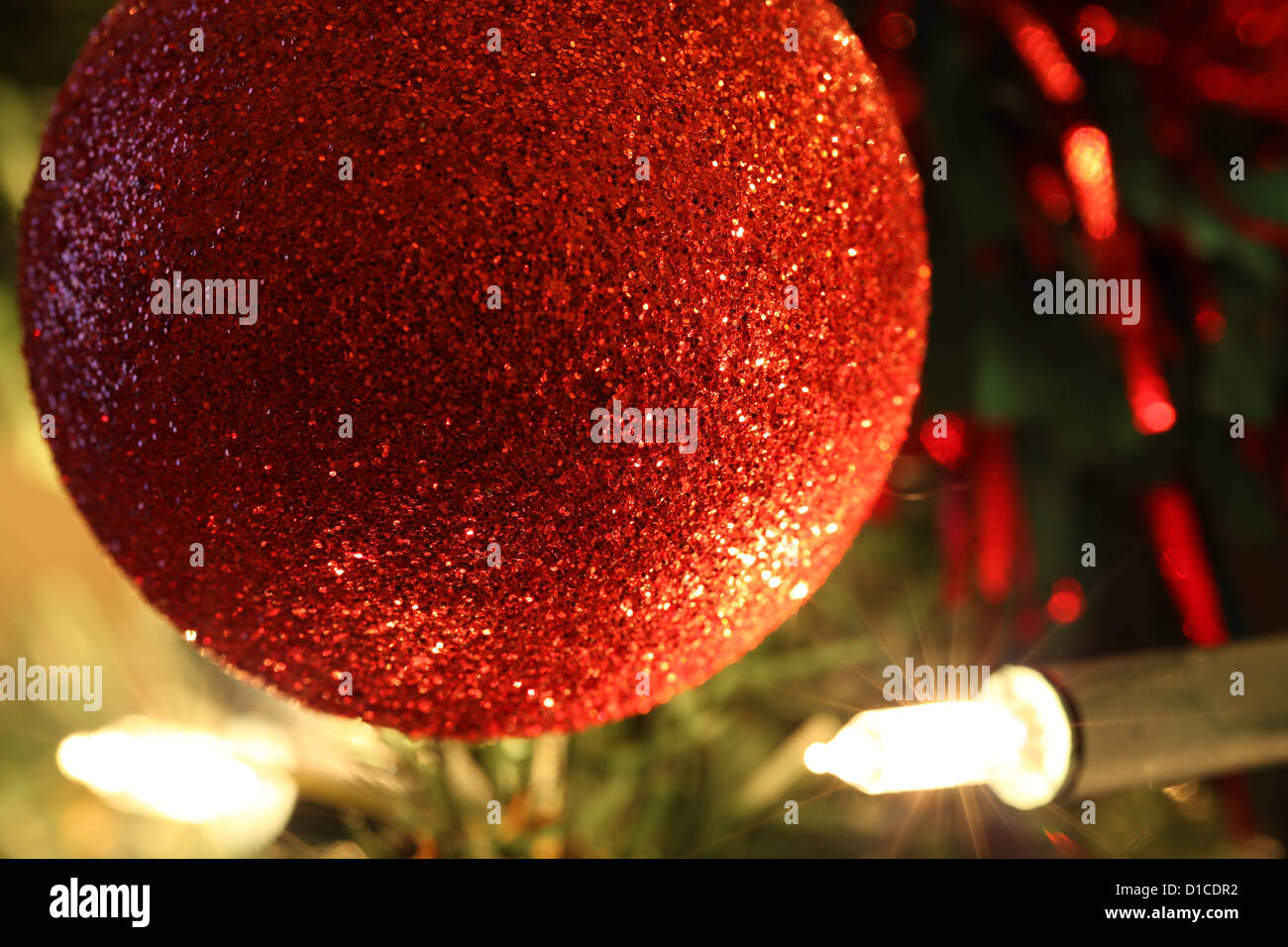 Red Christmas bauble hanging on an artificial tree with fairy lights in the background Stock Photo