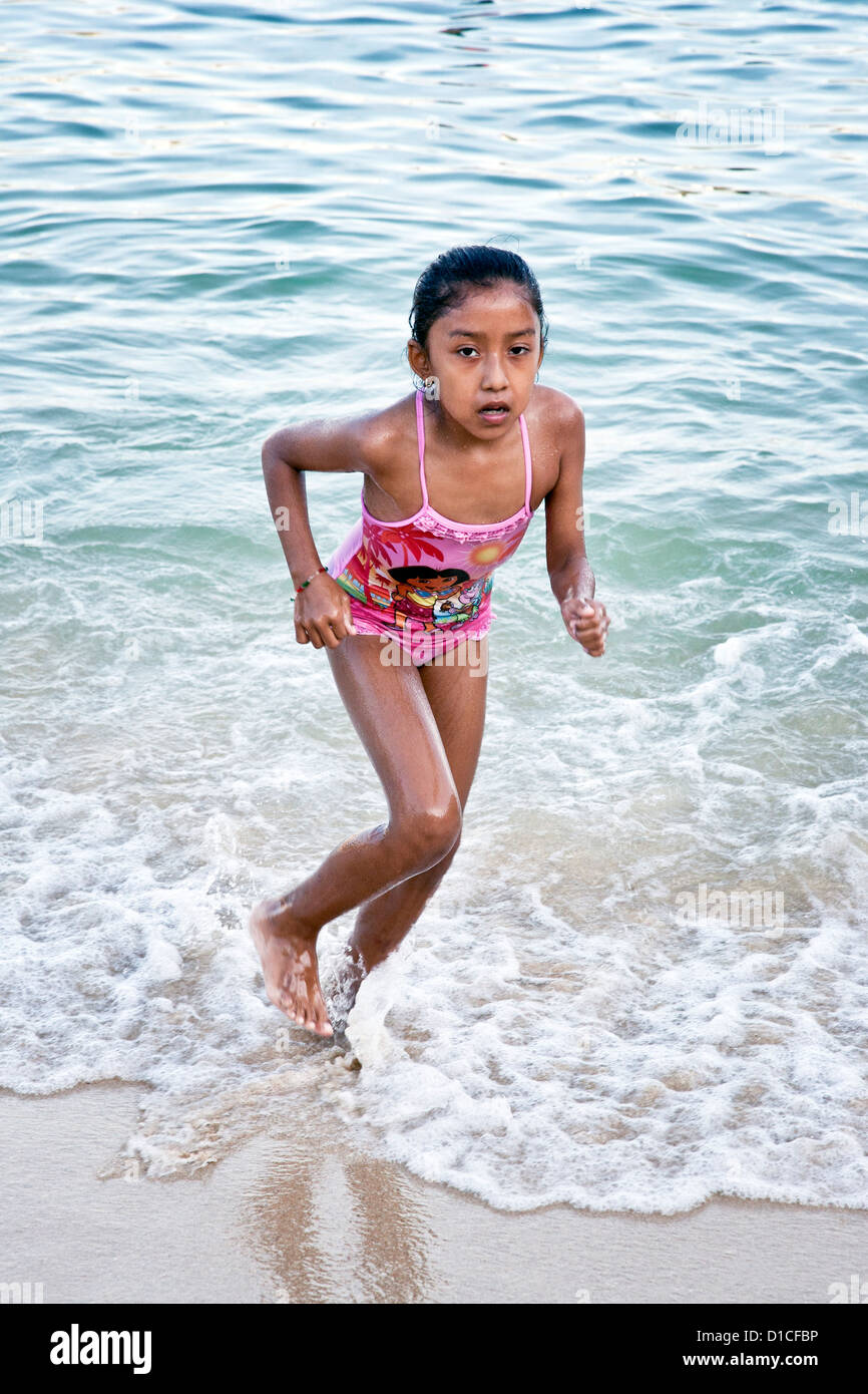 brown young Mexican girl in pink bathing suit running in surf at edge of playa Santa Cruz beach Huatulco Mexico Stock Photo