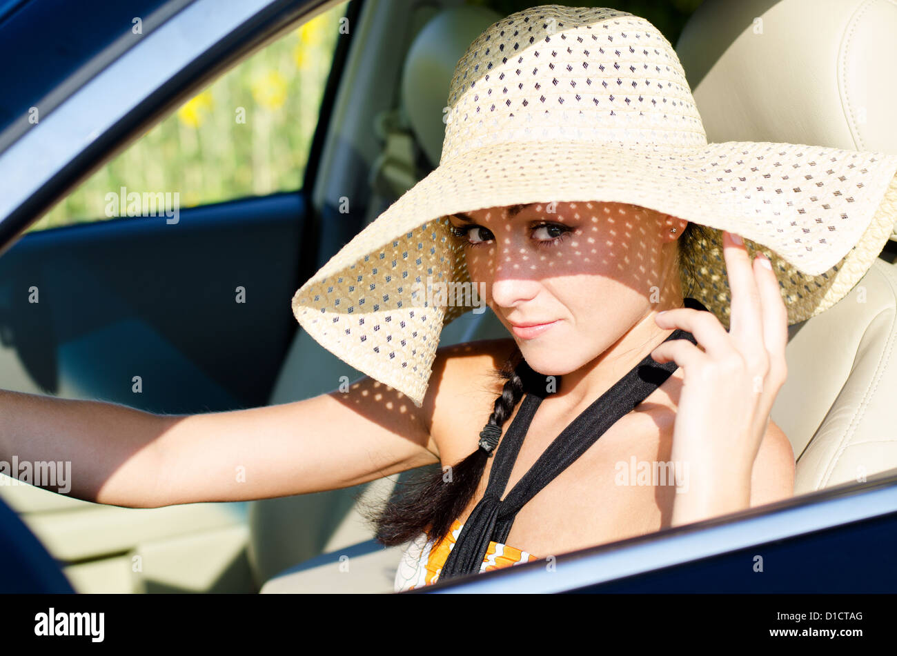 Beautiful woman driver in a large straw sunhat lifting up the wide brim with her fingers as she looks up out of the car Stock Photo