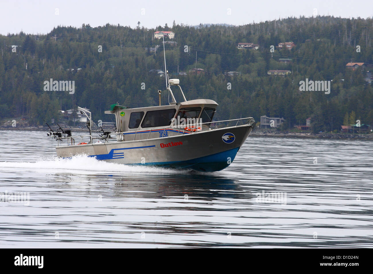 A sliver and blue fishing boat skimming across Alaskan waterway Stock