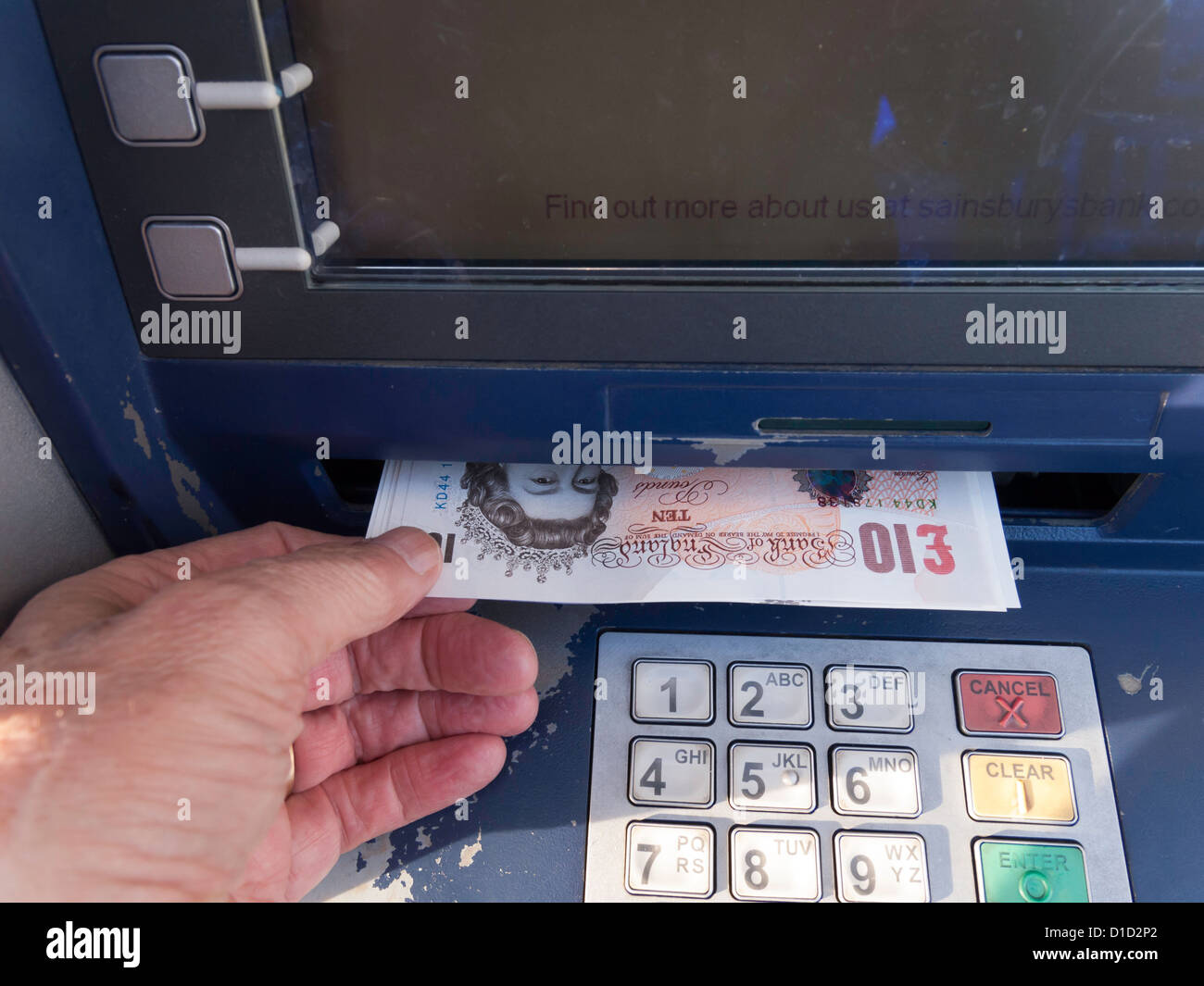 A man's hand taking £100 cash dispensed by a bank's ATM machine Stock Photo